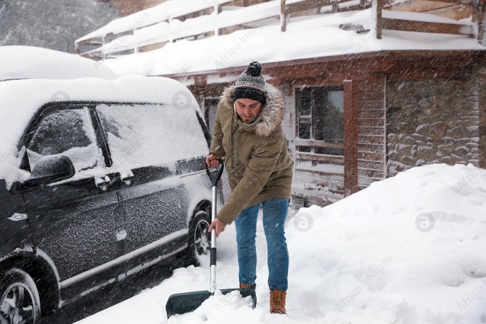 Photo of Young man cleaning snow with shovel near his house