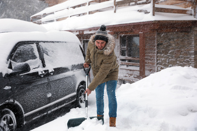 Photo of Young man cleaning snow with shovel near his house