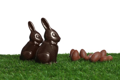 Photo of Chocolate bunnies and eggs on green grass against white background, space for text. Easter celebration