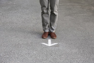Photo of Man standing near arrow on asphalt. Choice concept