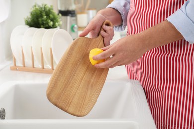 Man rubbing wooden cutting board with lemon at sink in kitchen, closeup