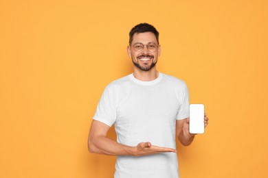 Photo of Happy man showing smartphone on orange background. Space for text