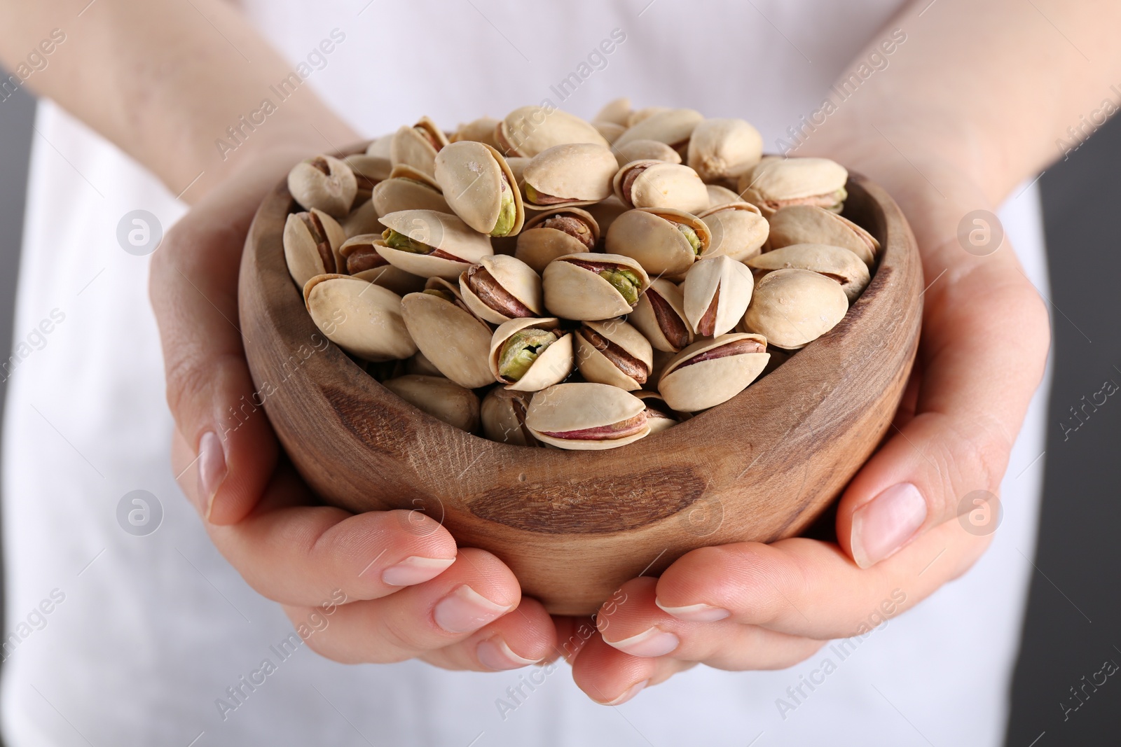 Photo of Woman holding tasty pistachios in bowl on grey background, closeup