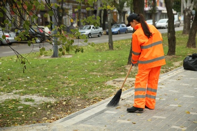 Photo of Street cleaner sweeping fallen leaves outdoors on autumn day