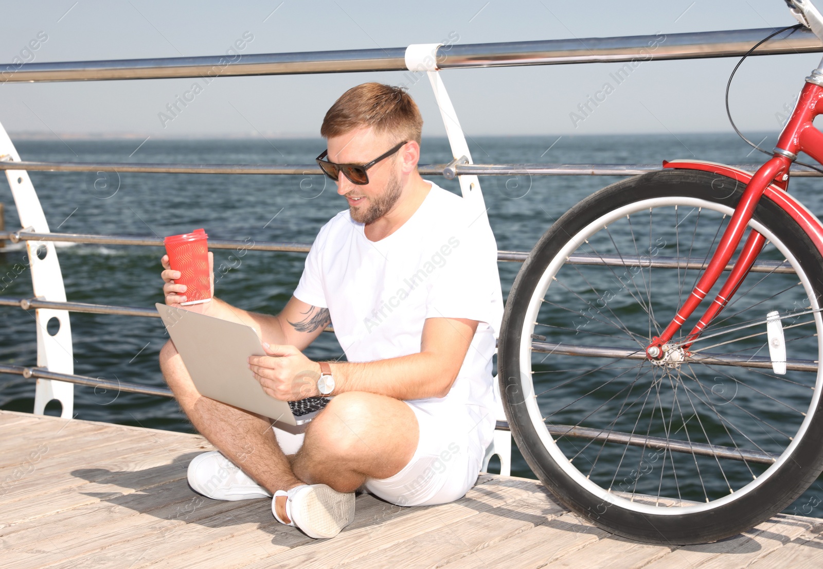 Photo of Attractive man with laptop and bike near sea on sunny day