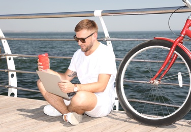 Attractive man with laptop and bike near sea on sunny day
