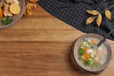 Photo of Flat lay composition with bowl of fresh homemade soup to cure flu and space for text on wooden background