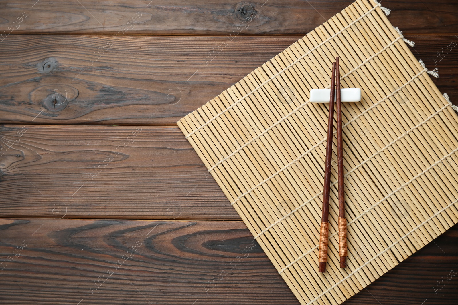 Photo of Bamboo mat with pair of chopsticks and rest on wooden table, top view. Space for text