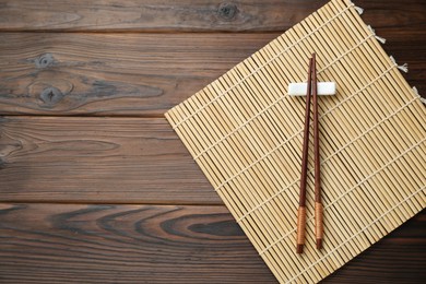Photo of Bamboo mat with pair of chopsticks and rest on wooden table, top view. Space for text