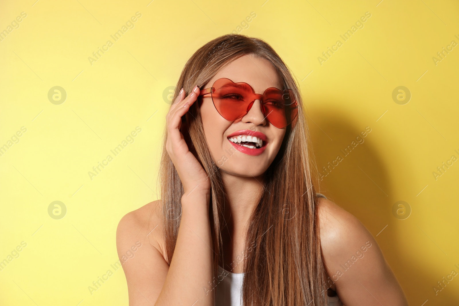 Photo of Young woman wearing stylish heart shaped sunglasses on yellow background