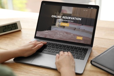 Image of Woman using laptop to book hotel at wooden table, closeup