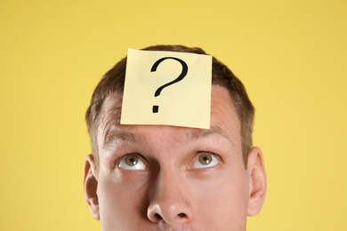 Emotional man with question mark on yellow  background, closeup