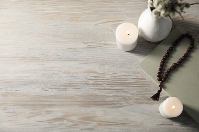 Photo of Rosary beads, burning candles and book on wooden table, flat lay. Space for text