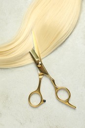 Professional hairdresser scissors with blonde hair strand on grey table, top view