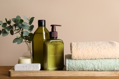 Photo of Solid shampoo bar and bottles of cosmetic product on wooden table near beige wall