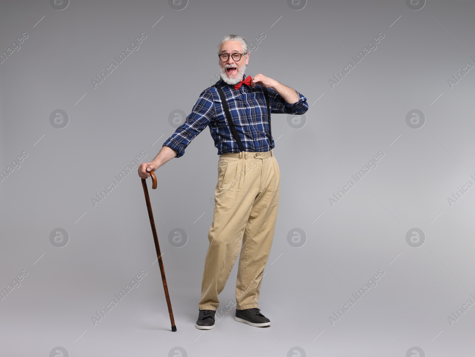 Photo of Cheerful senior man with walking cane on gray background