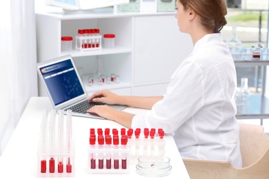 Test tubes with blood samples and scientist working on computer in laboratory