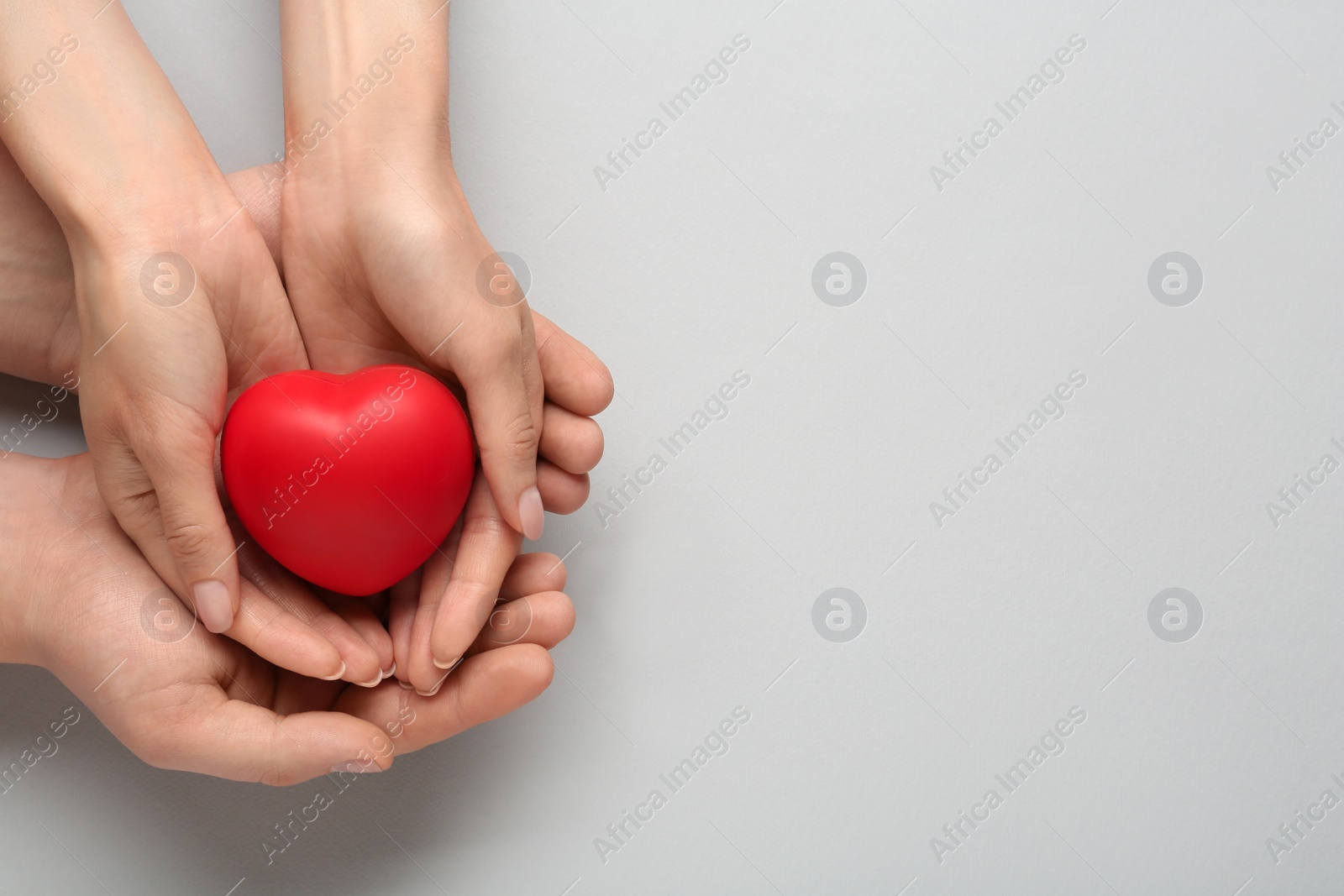 Photo of People holding red decorative heart on grey background, top view and space for text. Cardiology concept