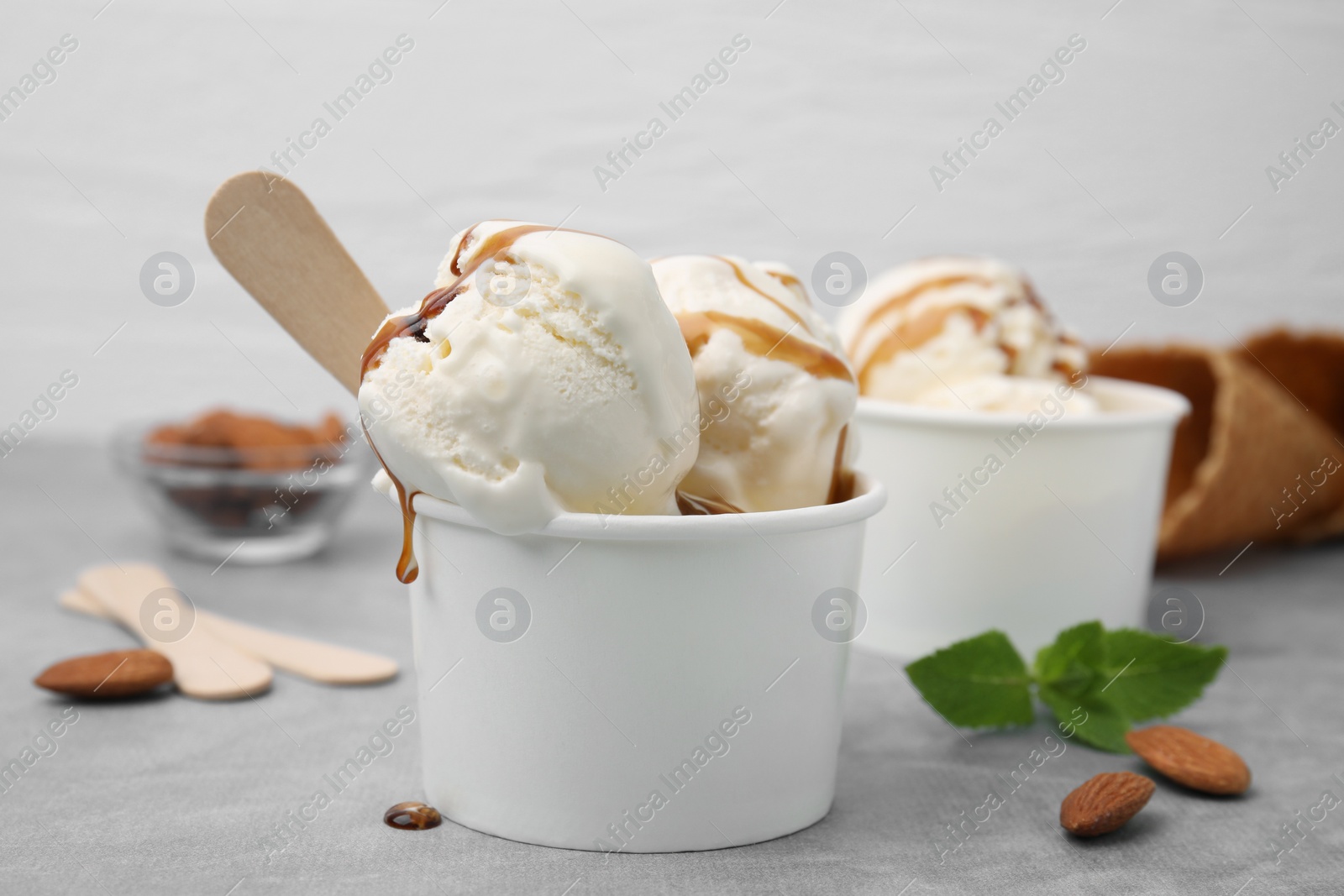 Photo of Scoops of ice cream with caramel sauce in paper cup on light grey table, closeup