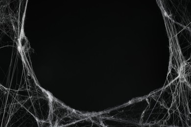 Photo of Creepy white cobweb on black background, space for text