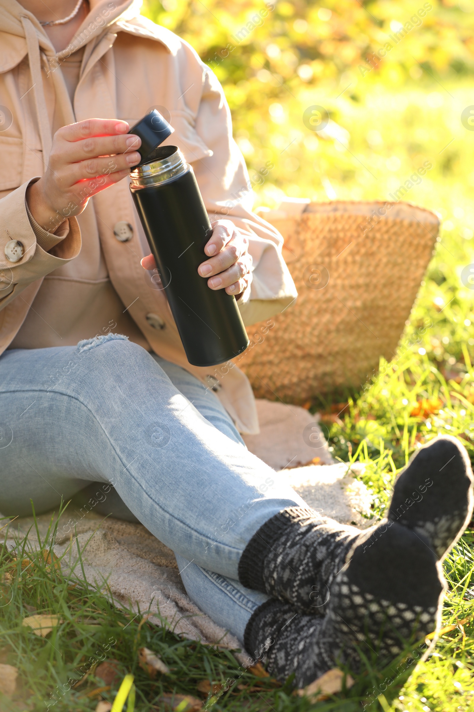 Photo of Picnic time. Woman opening thermos on green grass outdoors, closeup