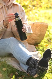 Photo of Picnic time. Woman opening thermos on green grass outdoors, closeup