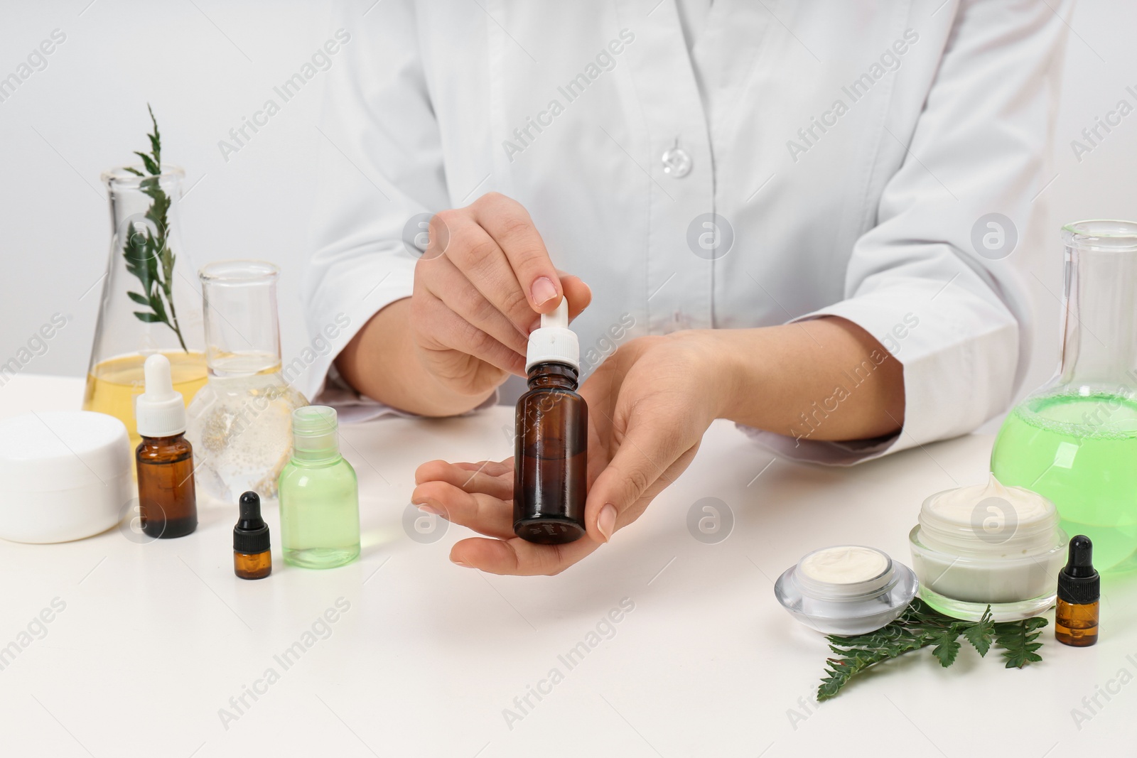 Photo of Female dermatologist holding bottle of skin care product at table, closeup