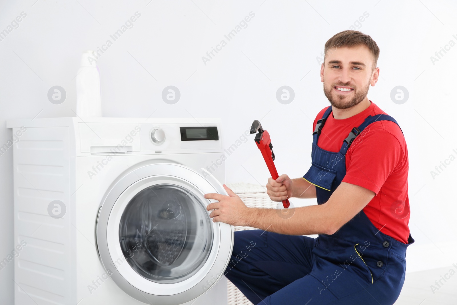 Photo of Young plumber with wrench near washing machine in bathroom