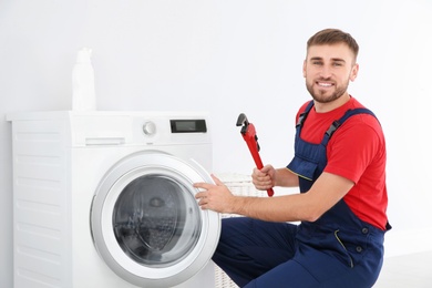 Young plumber with wrench near washing machine in bathroom