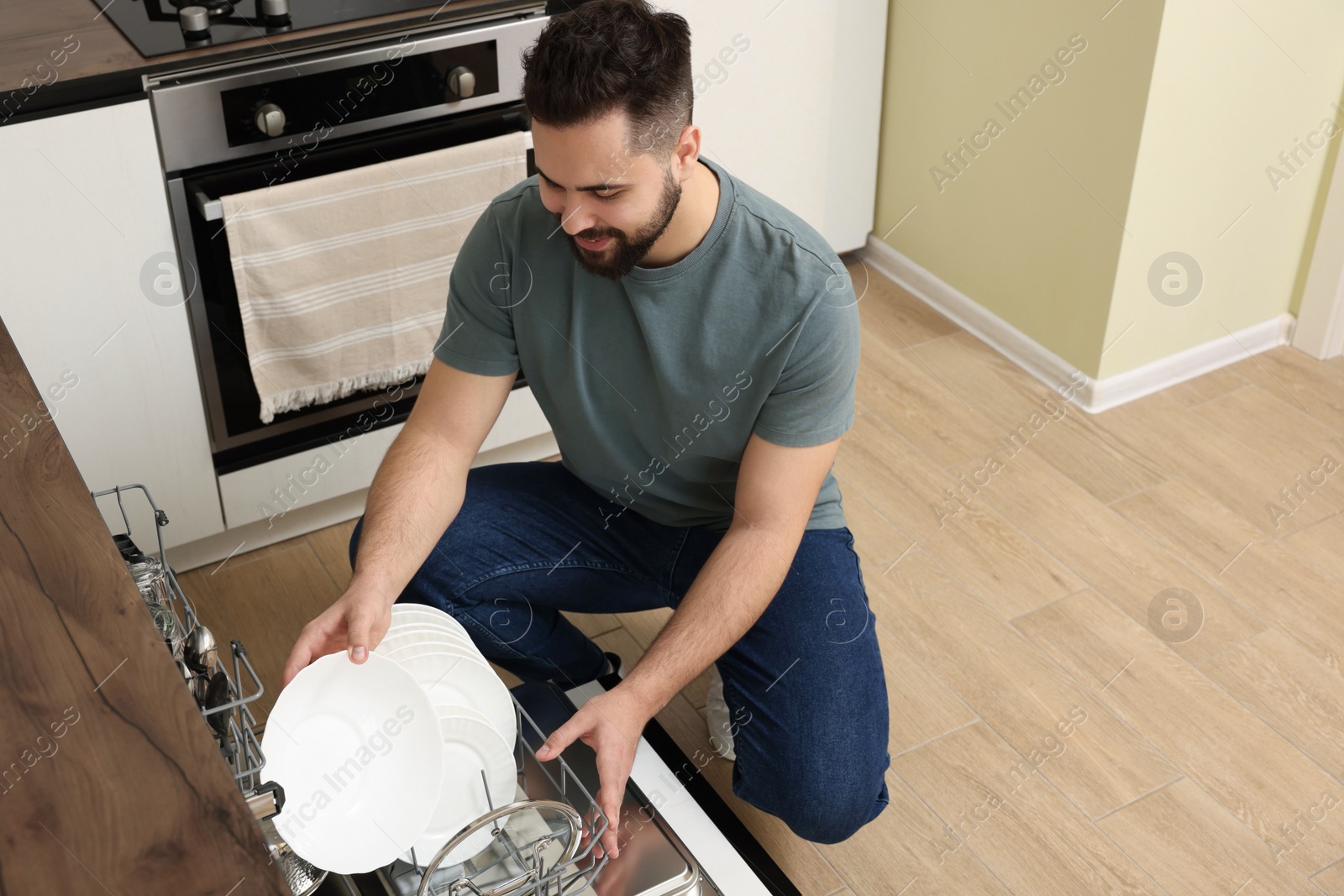 Photo of Smiling man loading dishwasher with plates in kitchen. Space for text