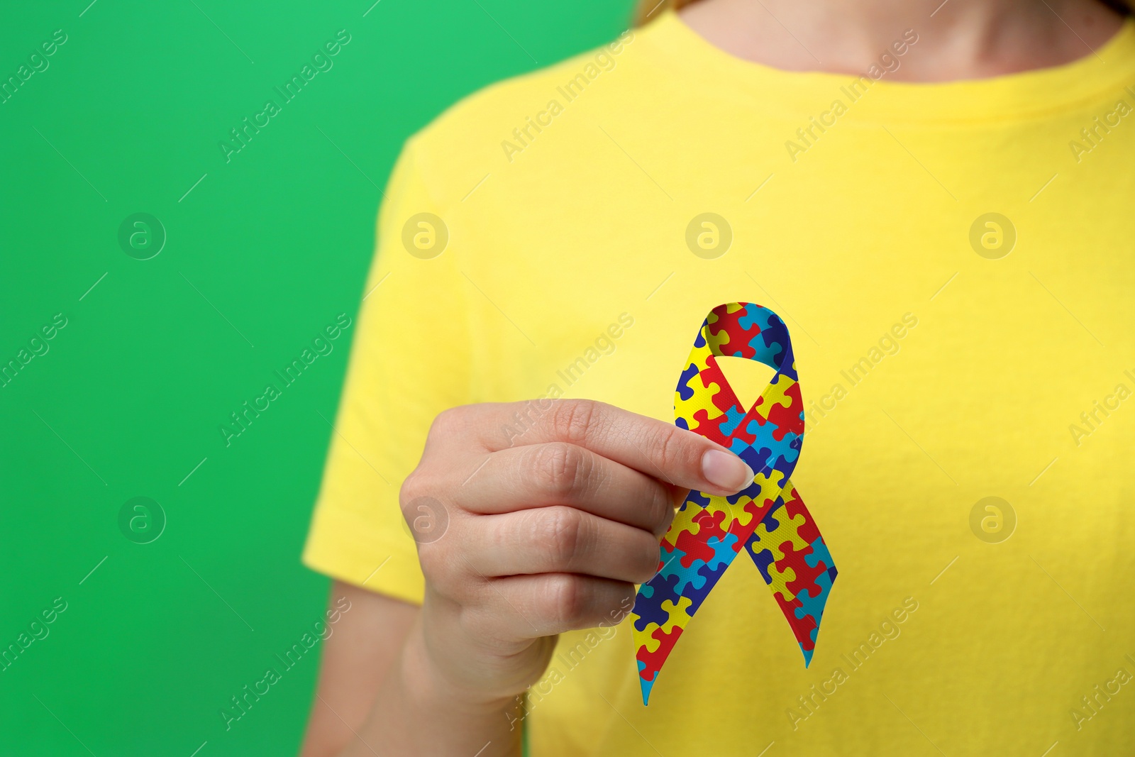 Image of World Autism Awareness Day. Woman with colorful puzzle ribbon on green background, closeup