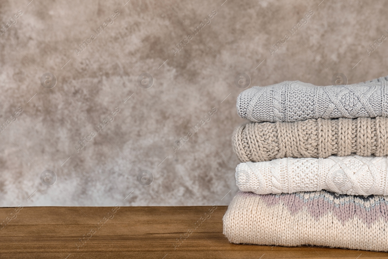 Photo of Stack of warm autumn clothes on wooden table. Space for text