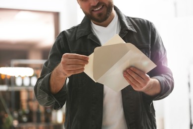 Man holding envelope with greeting card indoors, closeup