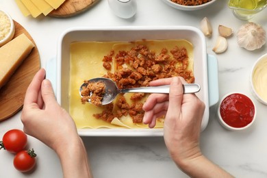 Woman making lasagna at white marble table, top view