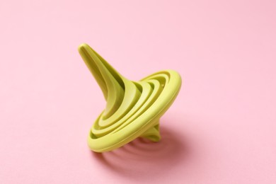 Photo of One green spinning top on pink background, closeup