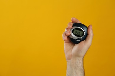 Man holding digital timer on yellow background, closeup. Space for text