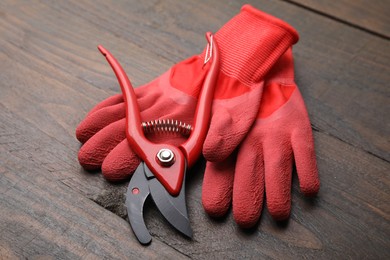 Photo of Pair of red gardening gloves and secateurs on wooden table