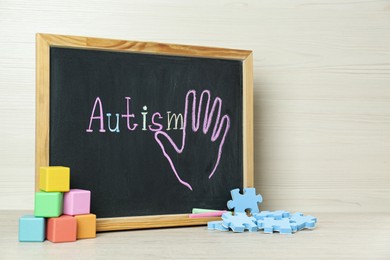 Photo of Chalkboard with word Autism, colorful cubes and jigsaw puzzle pieces on white wooden table