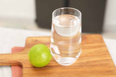 Photo of Filtered water in glass and lime on light table in kitchen, closeup