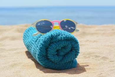 Photo of Towel with stylish sunglasses on sand near sea, closeup. Beach accessories