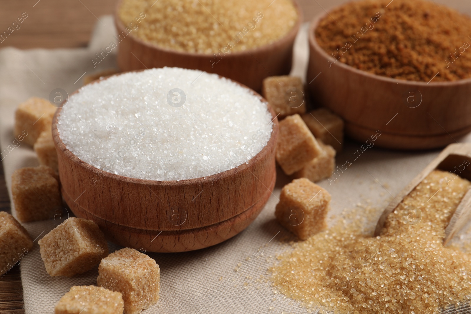 Photo of Different types of sugar in granules and cubes on cloth, closeup