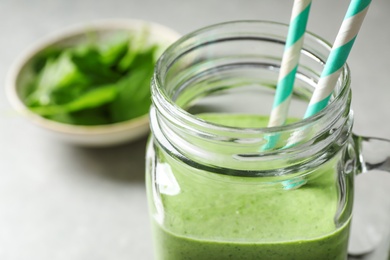 Photo of Mason jar of healthy green smoothie with fresh spinach on grey table, closeup view