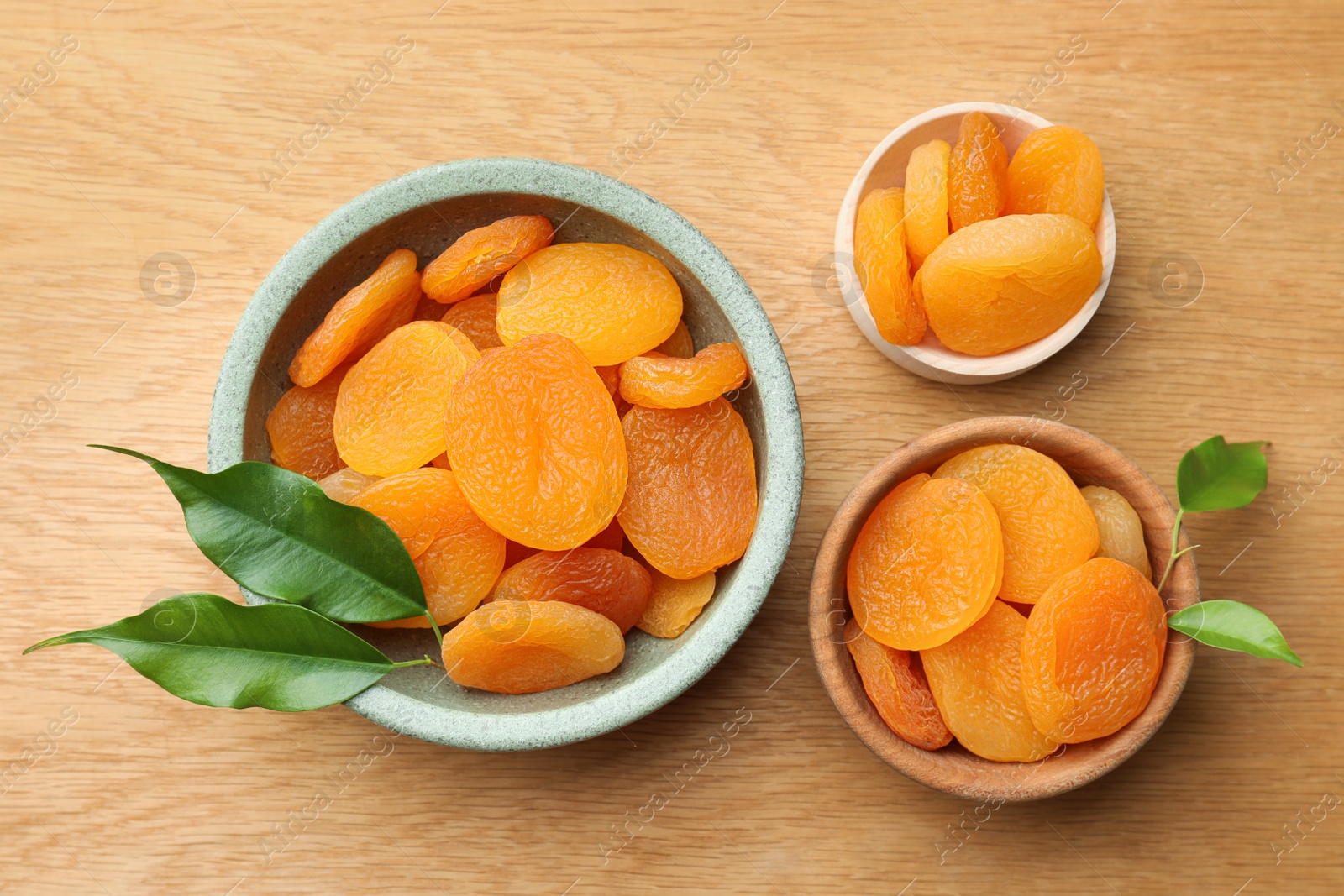 Photo of Tasty apricots with green leaves on wooden table, flat lay. Dried fruits