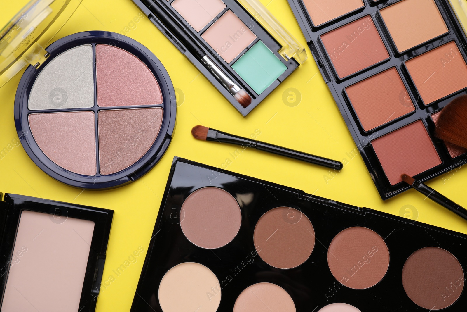 Photo of Different contouring palettes and brushes on yellow background, flat lay. Professional cosmetic product