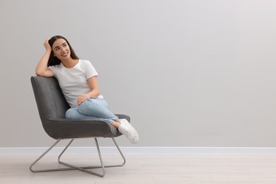 Photo of Beautiful woman sitting in armchair near light grey wall indoors, space for text