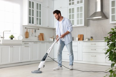 Photo of Happy man cleaning floor with steam mop in kitchen at home