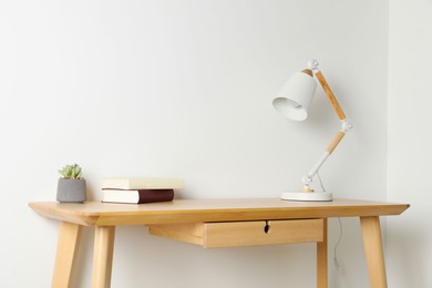 Photo of Stylish lamp, books and houseplant on wooden table near white wall. Interior design