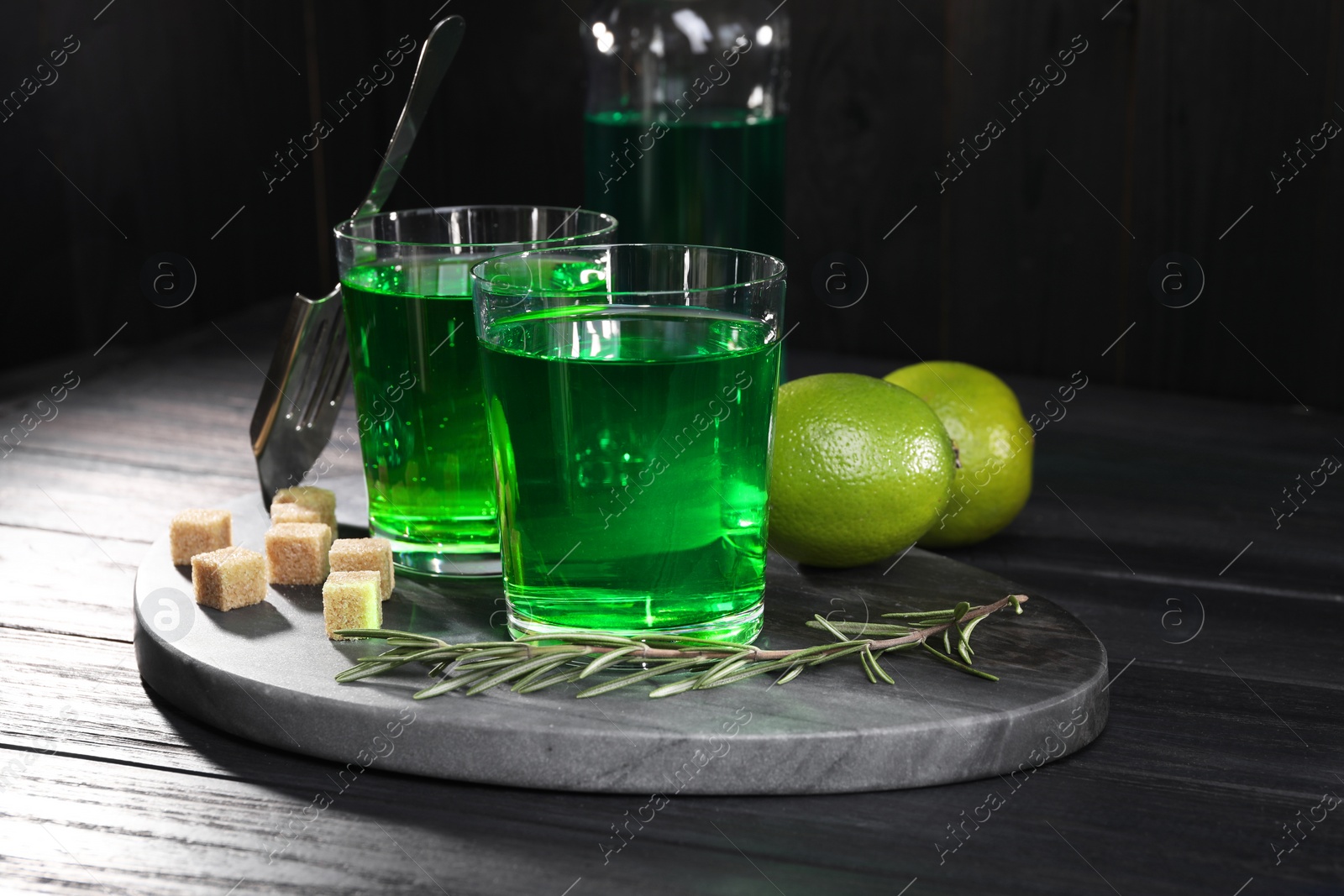 Photo of Absinthe in glasses, rosemary, brown sugar and lime on black wooden table. Alcoholic drink