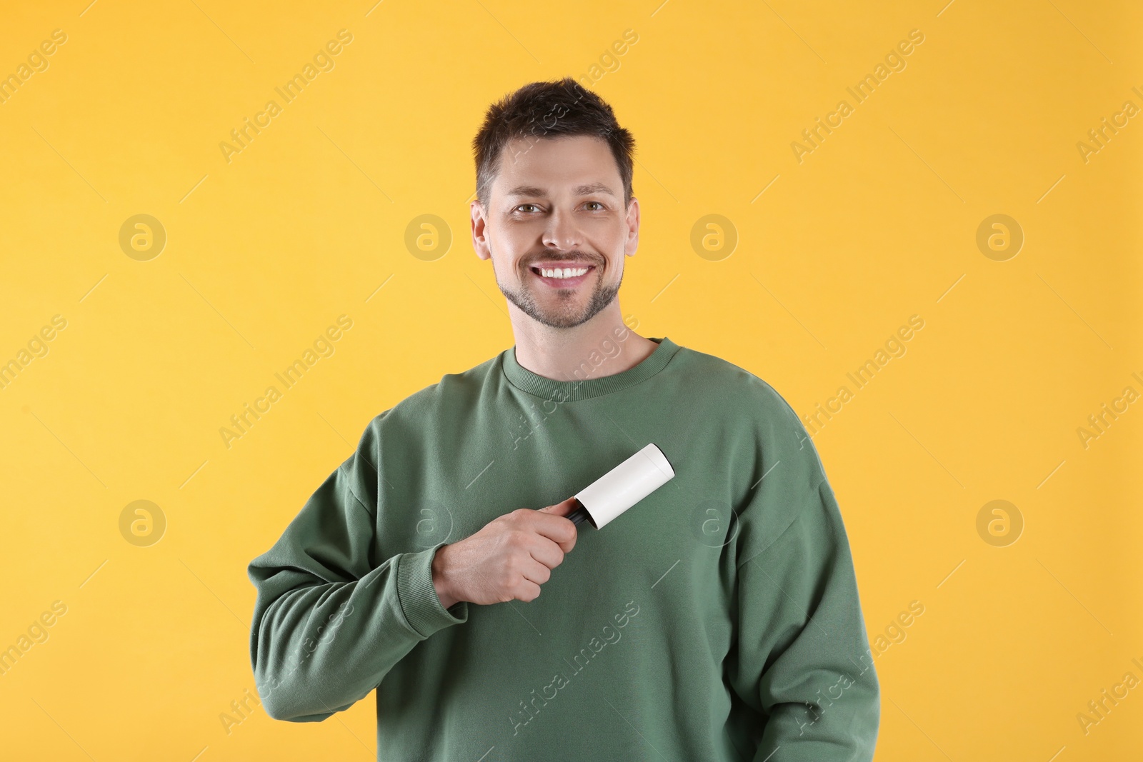 Photo of Man cleaning clothes with lint roller on yellow background