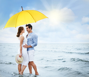 Happy young couple with umbrella for sun protection on beach near sea